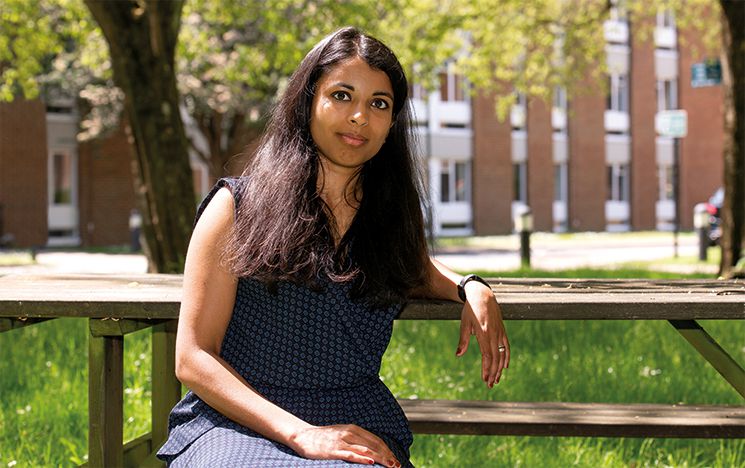 Suda sitting on a bench near a grassy area of campus