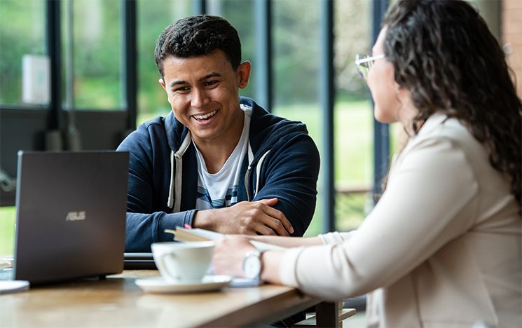 Two students chatting over coffee and a laptop