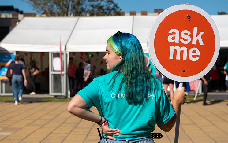 Student volunteer holding a sign saying 'ask me'