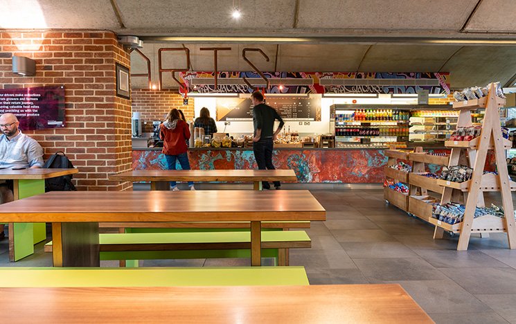 Inside of Arts Piazza cafe with two customers at the counter and an attendant serving them