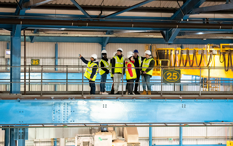 Six people wearing hard hats and high vis tour a factory