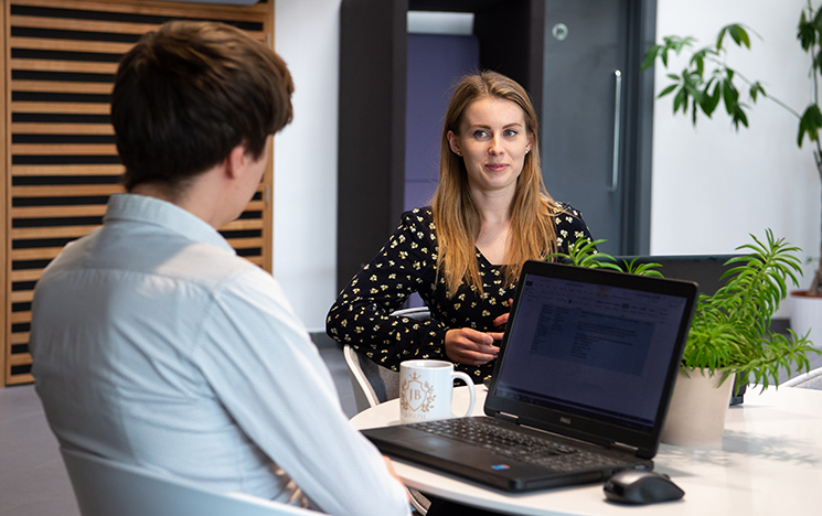 Two colleagues in a one-to-one meeting sat at a table looking at a laptop