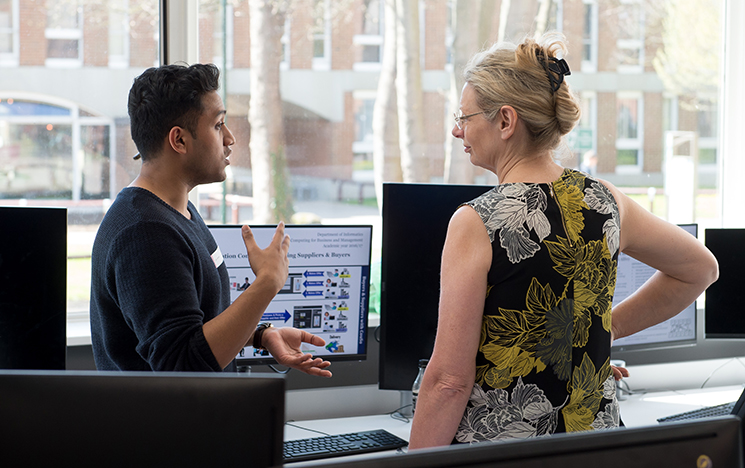 Two members of staff discuss a project standing in front of a computer