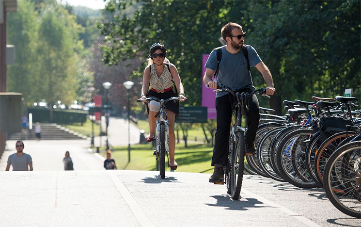 Two people cycling on campus on a sunny day