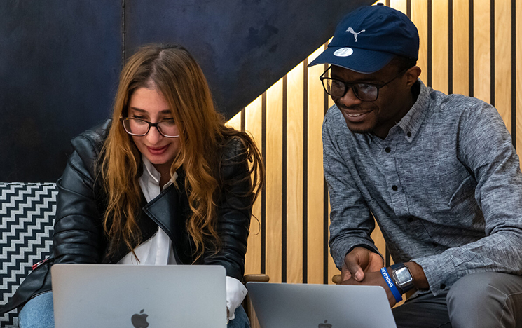 Two students sitting together at a table looking at their laptops