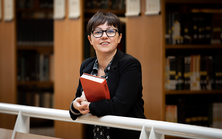 Image of Grazia Ragone leaning on bannister and holding a book