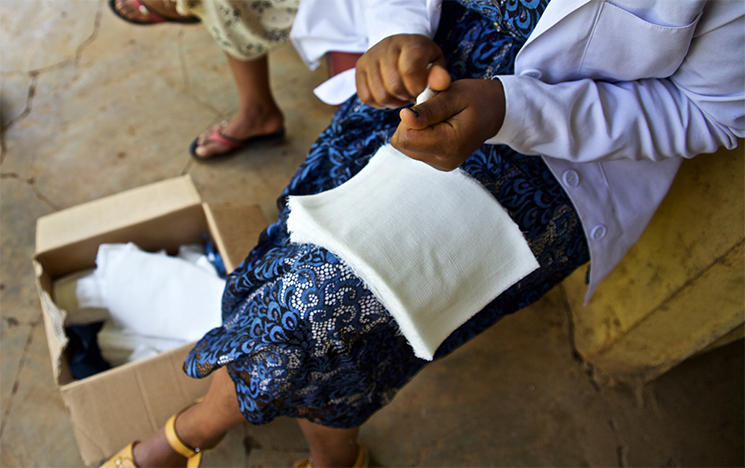Person sits on a chair with a box of medical supplies by her feet. They are adding dressings to the box.