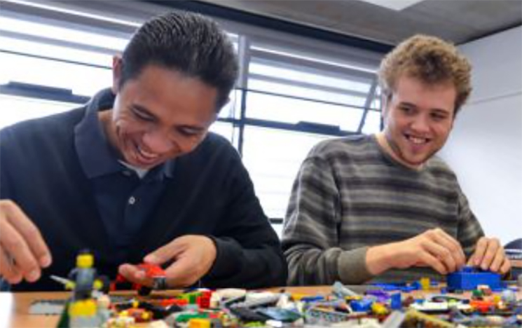 Two people sit at a table playing with children's toys