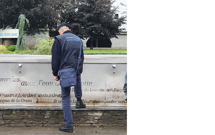 A Lourdes volunteer (hospitalier) collects Lourdes spring water from a tap.