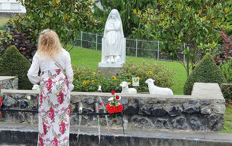 Prayers and flowers in front of a statue of St Bernadette.