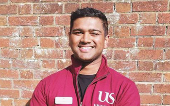 Nunkeshwar (Adarsh) Ramdawor wearing a Sussex hoodie and standing in front of a red brick wall