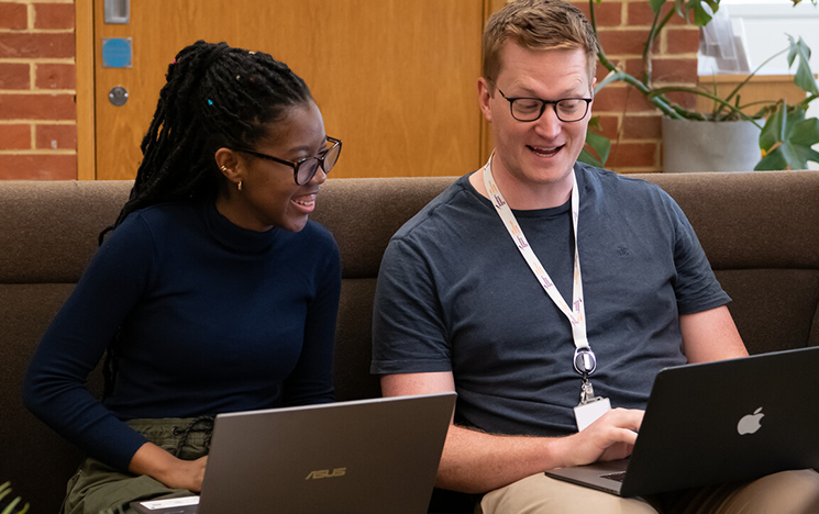 Two students sitting in the library with laptops on their laps.