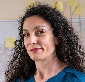 Headshot photo of Dr Sarah Scuzzarello standing in front of post-it notes on a whiteboard