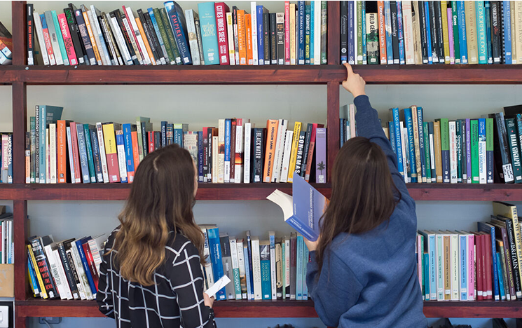 Two students with their backs to the camera choosing books in a library