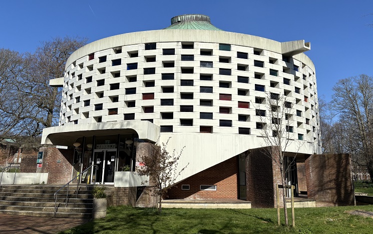 A circular modernist white building with many rectangular windows set into its walls