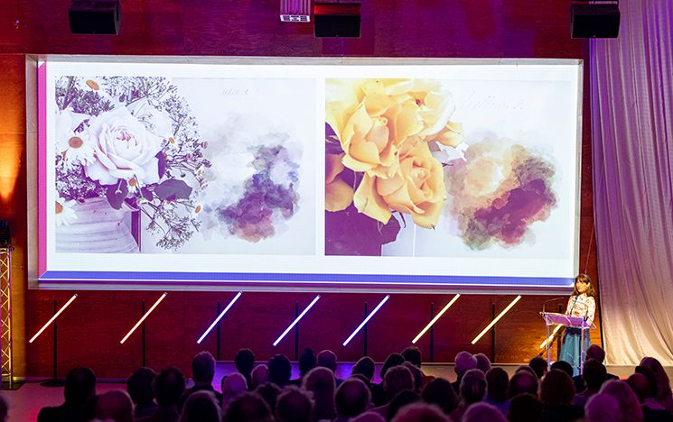 Alexandra Loske speaking on stage at Mondrian Lecture, with a large image of colourful flowers projected behind her. Image credit: Anne Reitsma