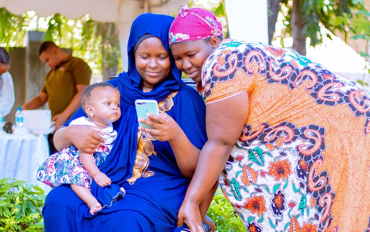 Two women, one sitting with a baby on her lap, looking at a mobile phone