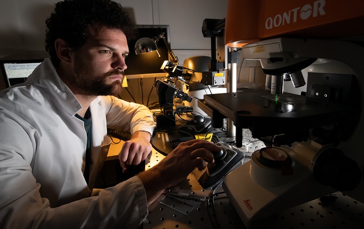 A scientist wearing a white coat moving a dial on a machine in a lab
