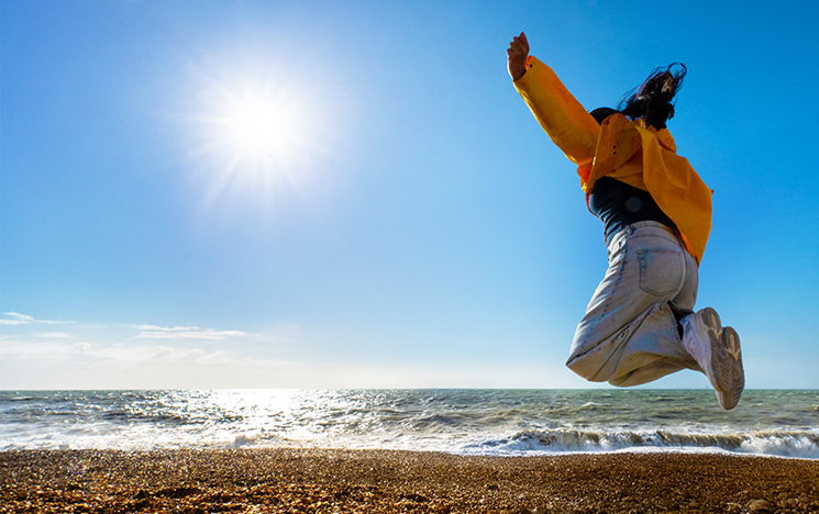 Person in orange jacket jumping enthusiastically on sunny Brighton beach