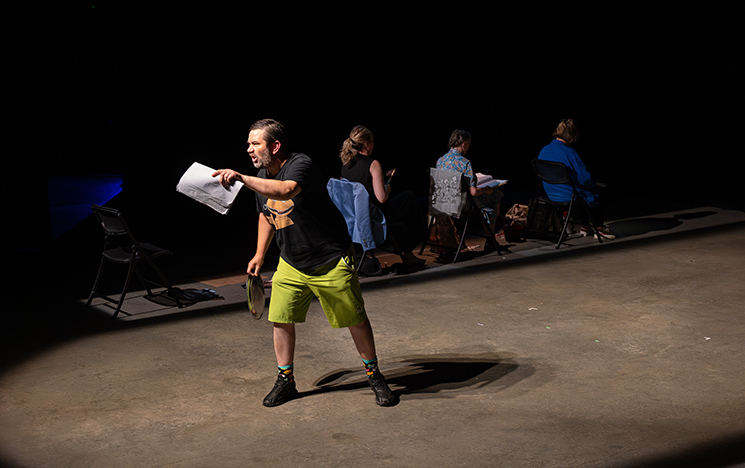 One actor centre-stage, and others seated behind, during a scene of Between the Acts performed at ACCA