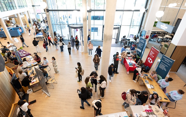 View looking down into the Student Centre atrium, a bright space with big windows and students clustering around a range of stalls