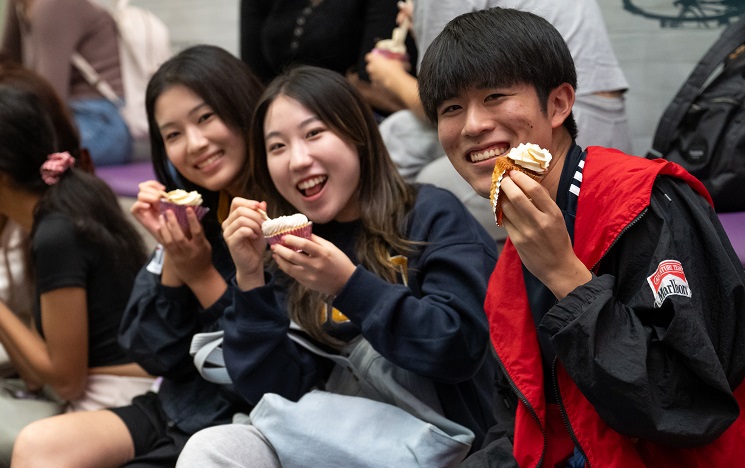 Three students sitting in a row laughing and showing off iced cupcakes