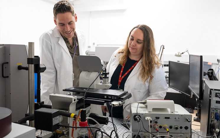 Two scientists wearing white coats smiling as they use Raman equipment