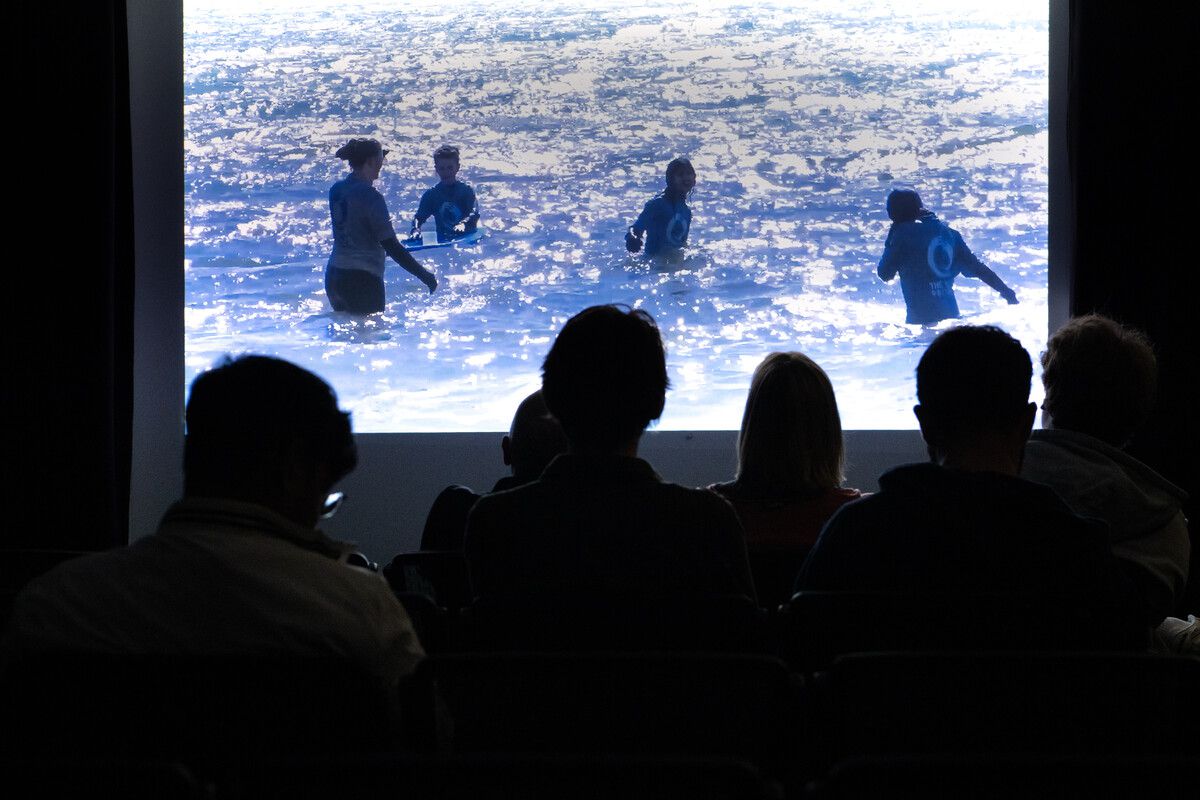 Students silhouetted, watching a film screening of people in the ocean