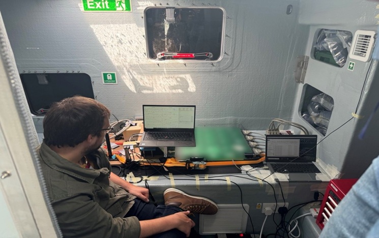 Photo of Dr Thomas Coussens, working with a laptop on a navy ship.