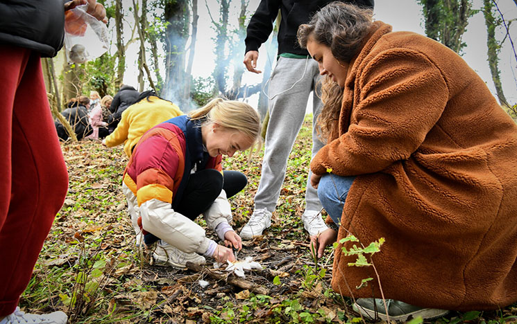 Two people collaborating in the Forest School to start a fire.