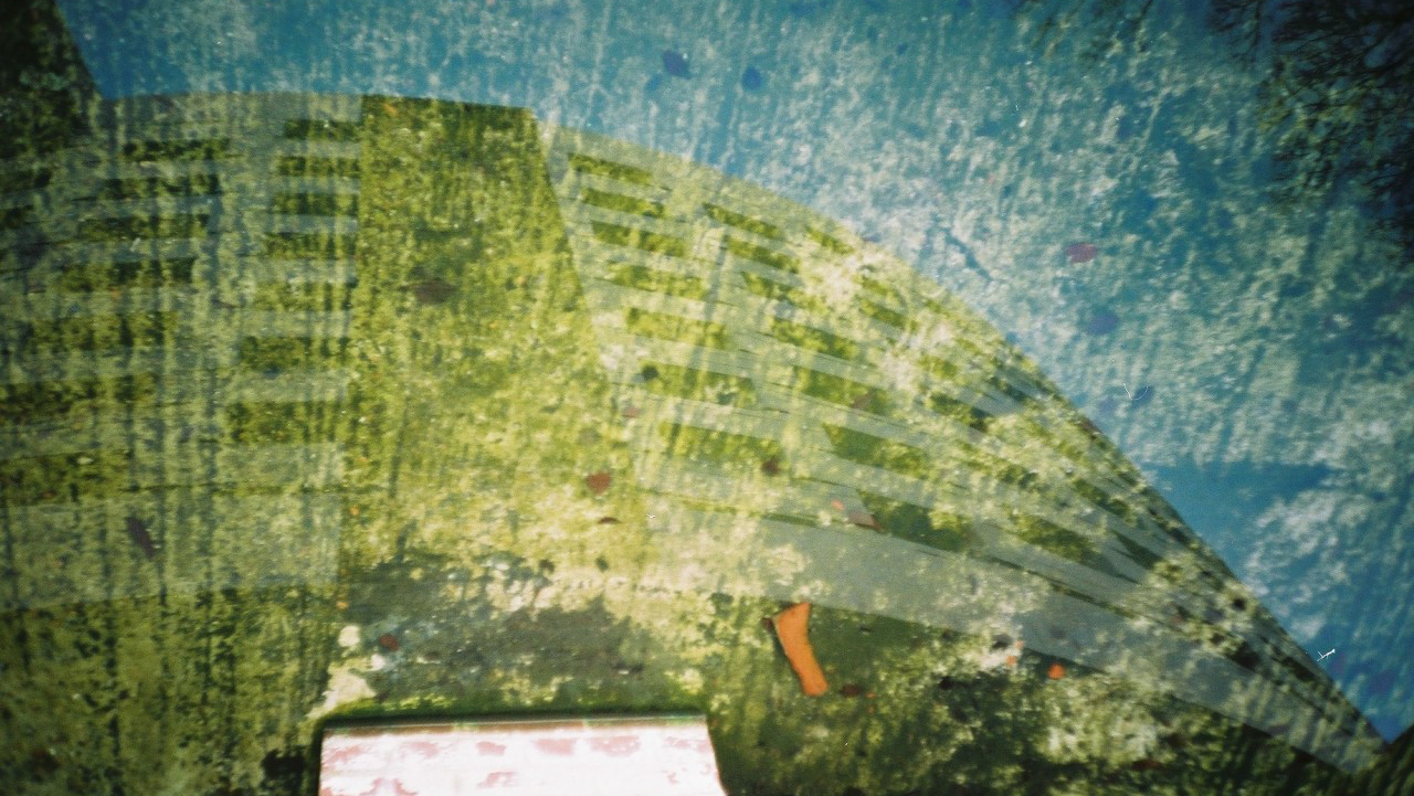 A distorted, abstract view of The Meeting House on Sussex campus reflected in water, with green and blue hues.