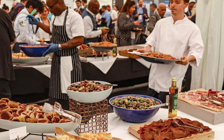  Food on table with chefs holding dishes and people in the background