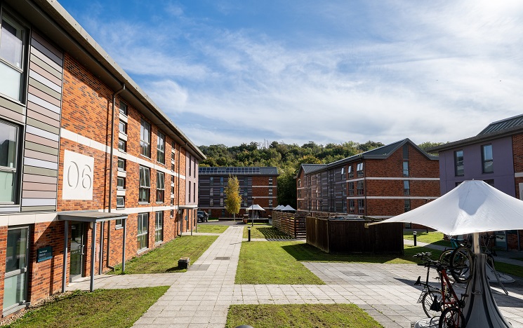 Pathways leading through grassy courtyard to student accommodation blocks, with bike parking and shade umbrellas