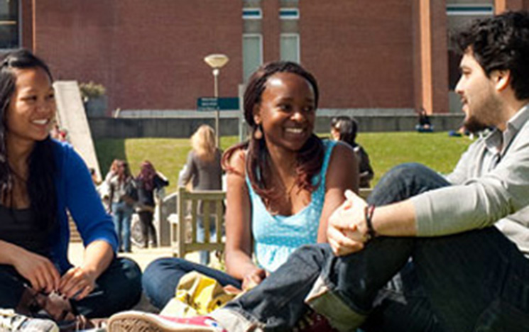 Three people sitting and chatting on a sunny campus.