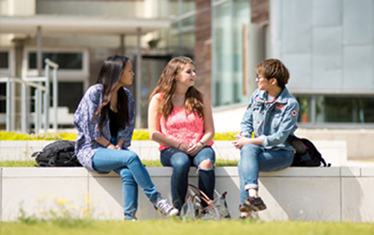 Three people sitting and chatting on campus.