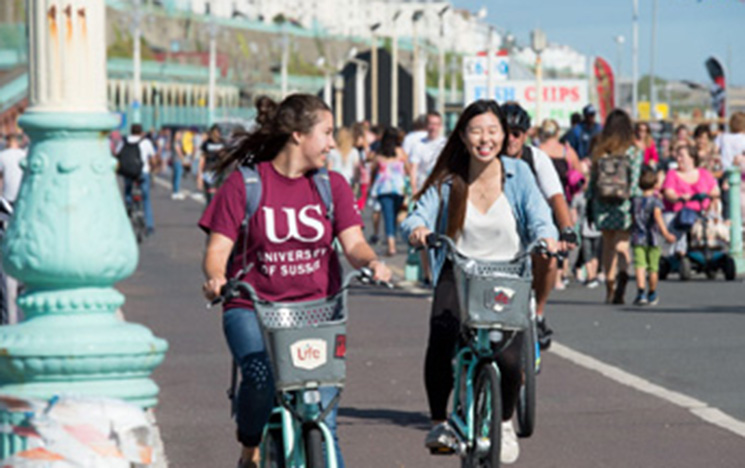 Photo of two students cycling on Brighton seafront.