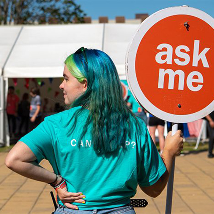 Student volunteer at open day holding 'ask me' sign