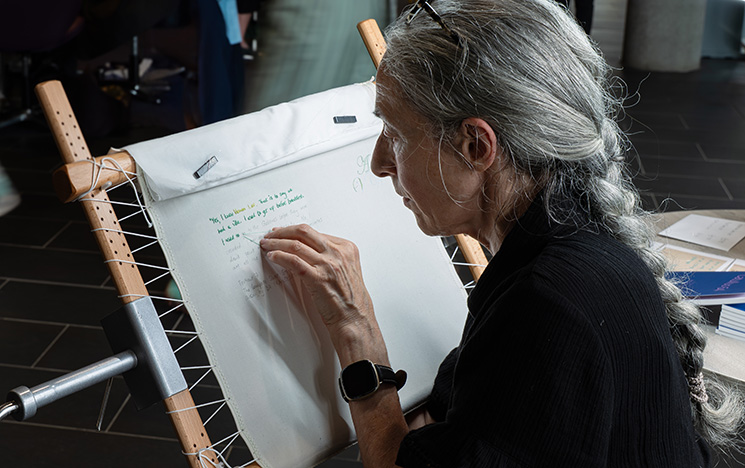 Andrea Mindel embroidering words onto a stretched piece of fabric.