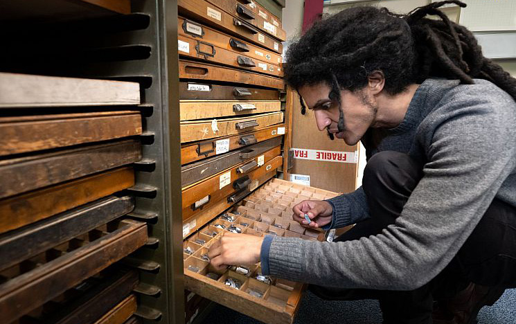 Person selects lettered pieces from a set of wooden drawers for the printed press.