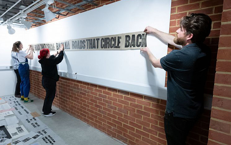Three people positioning printed paper on a wall.