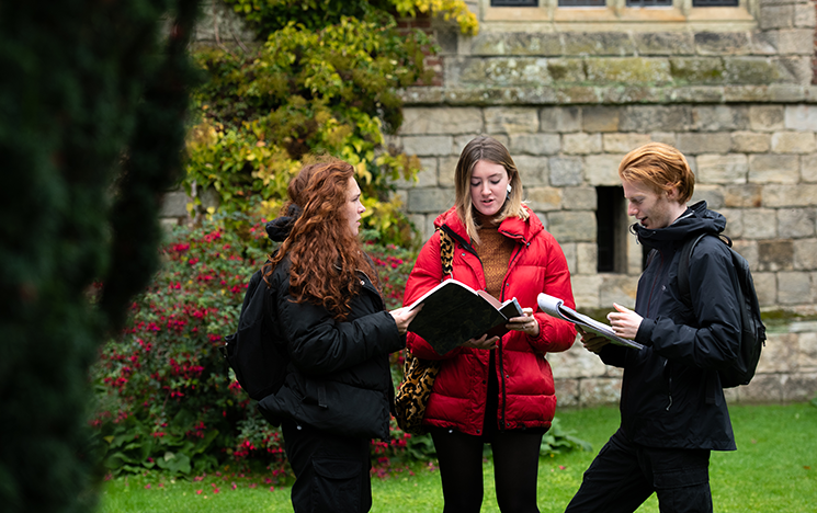 Three students discuss book material in front of an old building