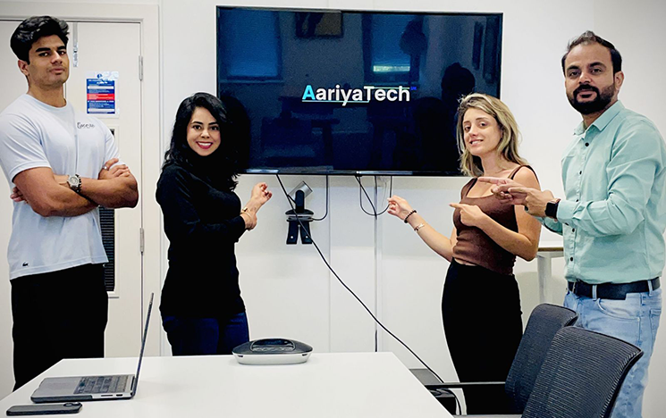 A group of two men and two women stood by a wall screen that says ArriyaTech.