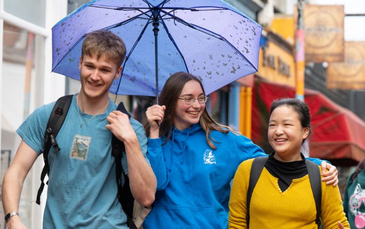 Three students share a laugh on a rainy day in Brighton