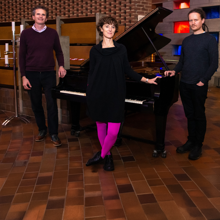 Three staff members pose in front of a piano
