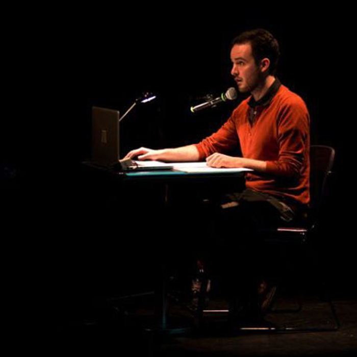 Augusto Corrieri playing the piano in a dark room, lit by a spotlight