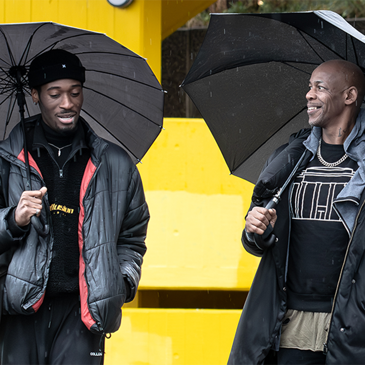 Topher Campbell and Jordi M. Carter chatting and each holding a large umbrella