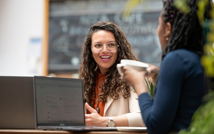 An advisor using a laptop, laughing with someone holding a teacup