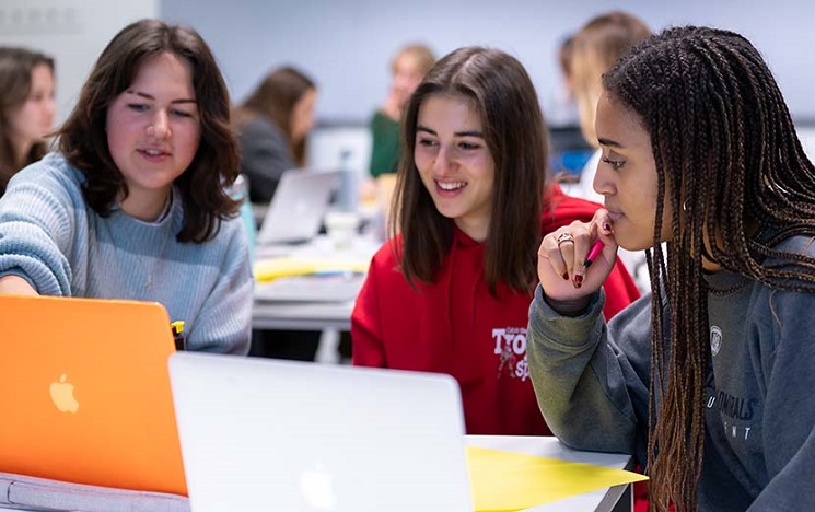 Three students around a table discussing something on a laptop