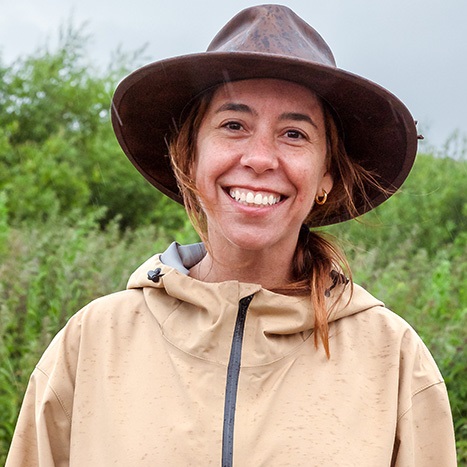 Smiling woman wearing coat and hat standing by a field