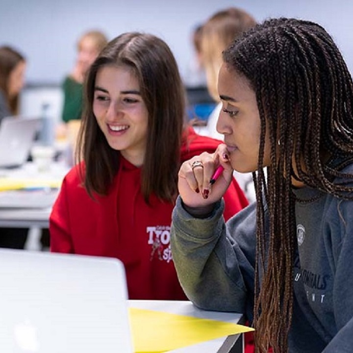 Three students around a table discussing something on a laptop